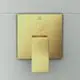 Goldene Badarmatur von Ideal Standard, flache rechteckige Steuerung mit Hebel und Rundknopf, montiert an heller Wand.